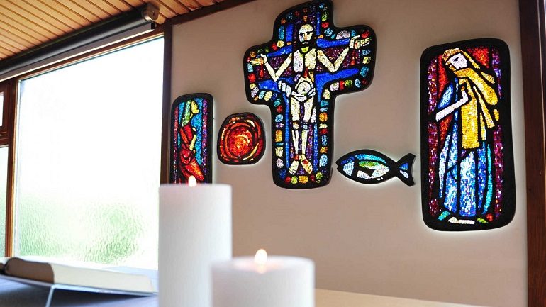 Foto von brennenden Kerzen und Blick auf bunte Glasbilder, in der Mitte Jesus am Kreuz (Foto epd uschmann)